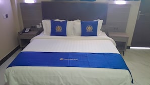 A hotel room with a bed, two pillows with a crest, a bedside phone, and a nightstand.