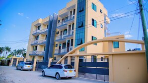 A multi-story building with balconies, a gated entrance, and parked cars.