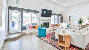 Een ruime woonkamer met een open haard, een grote flatscreen-tv aan de muur en een gezellige zithoek met een bank en fauteuils.