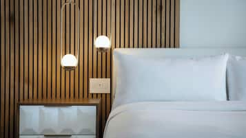 A neatly made bed with white linens, a wooden slatted headboard, and a bedside table with a drawer. Two wall-mounted lights are visible.