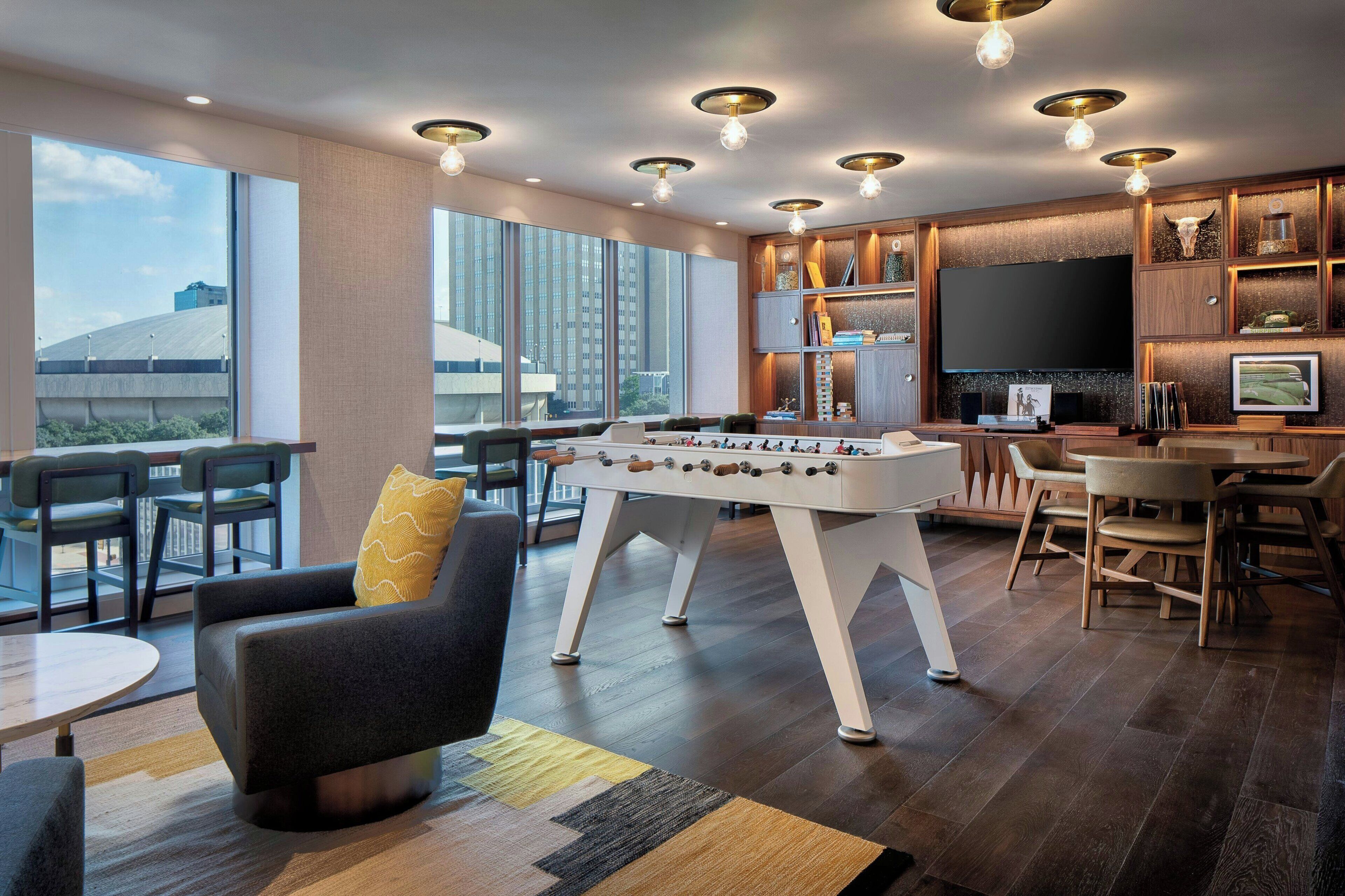 Een moderne woonkamer met een tafelvoetbaltafel, comfortabele zitplaatsen, een grote televisie en uitzicht over de stad.