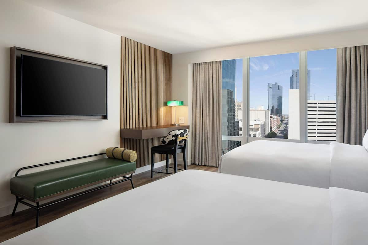 Een hotelkamer met een bed, een bureau, een stoel, een televisie en uitzicht op de stad.