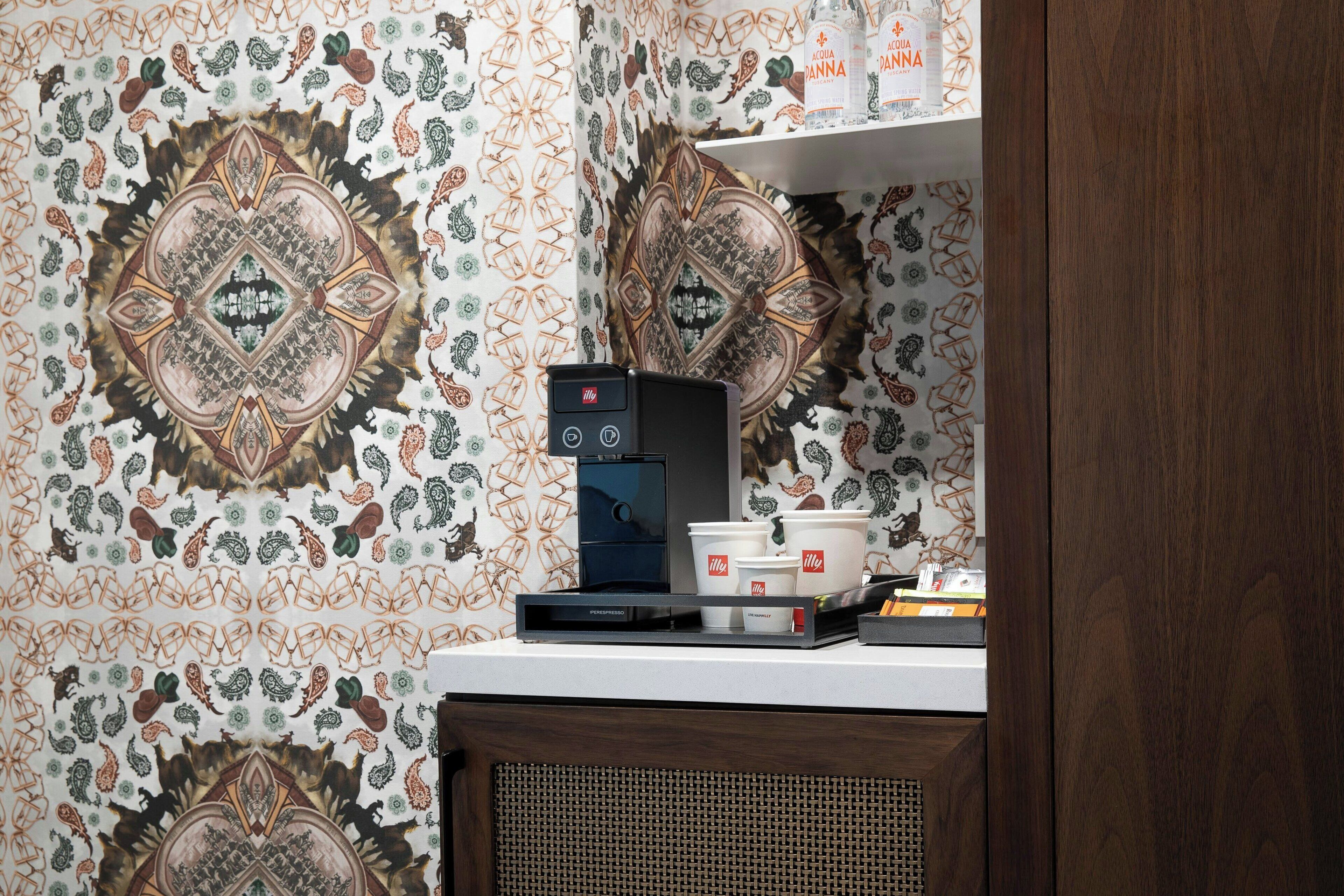 Une machine à café posée sur un comptoir, avec un papier peint à motifs et une étagère au-dessus.