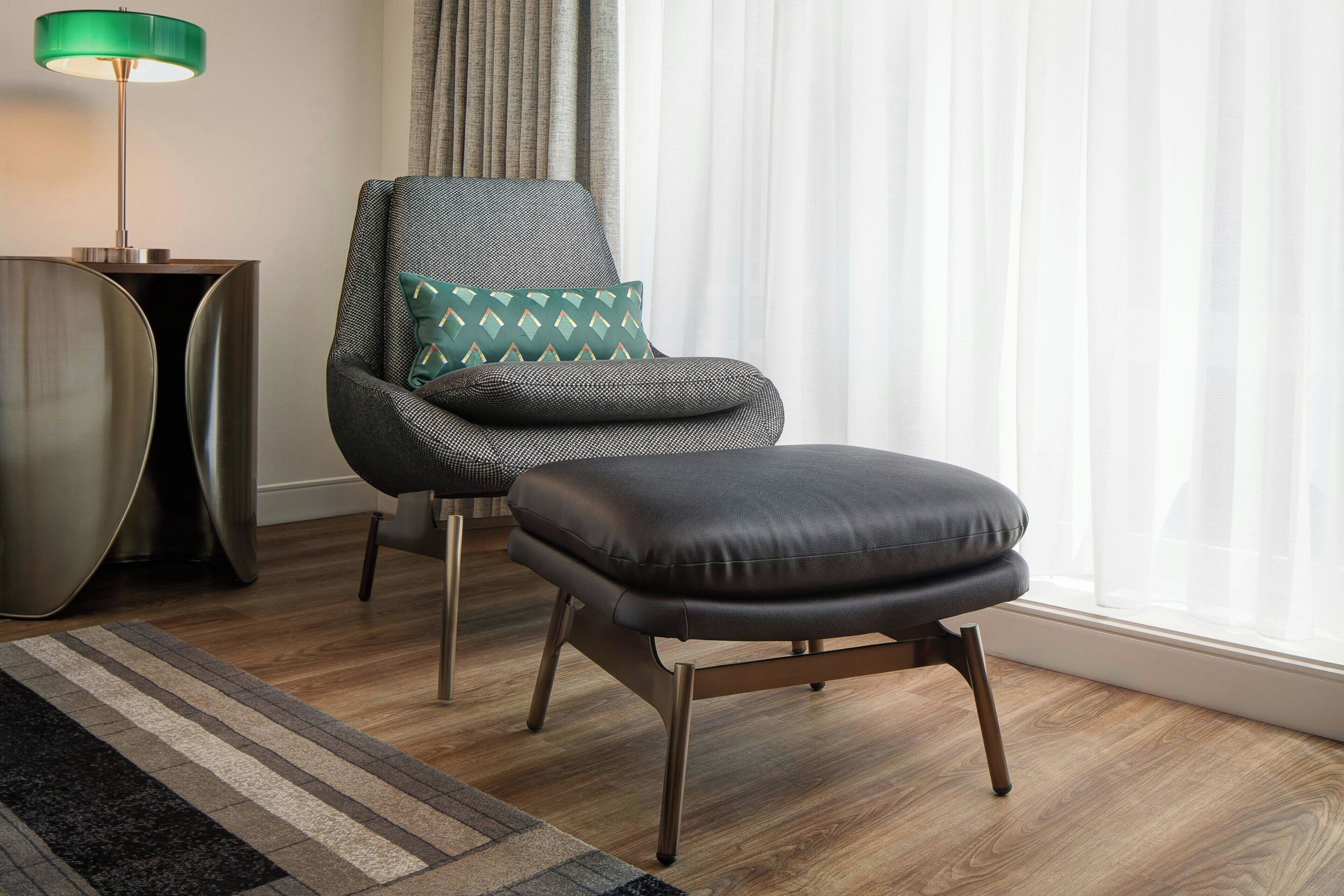 A modern living room with a leather ottoman, a patterned armchair, and a metallic side table.