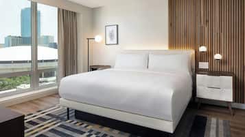 Habitación de hotel moderna con una cama grande, una mesita de noche, una lámpara de pie y vista a la ciudad.
