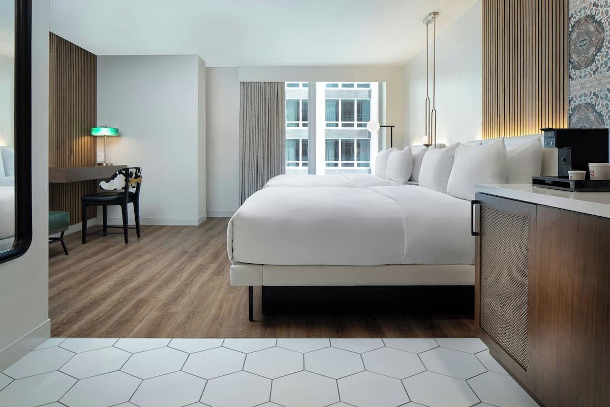 Een hotelkamer met een groot bed, een bureau met een stoel, een raam met gordijnen en uitzicht op buiten.