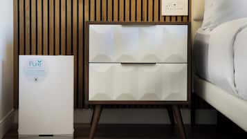 A modern bedroom with a white bed, a nightstand with a white drawer, and a Pure wellness air purifier.