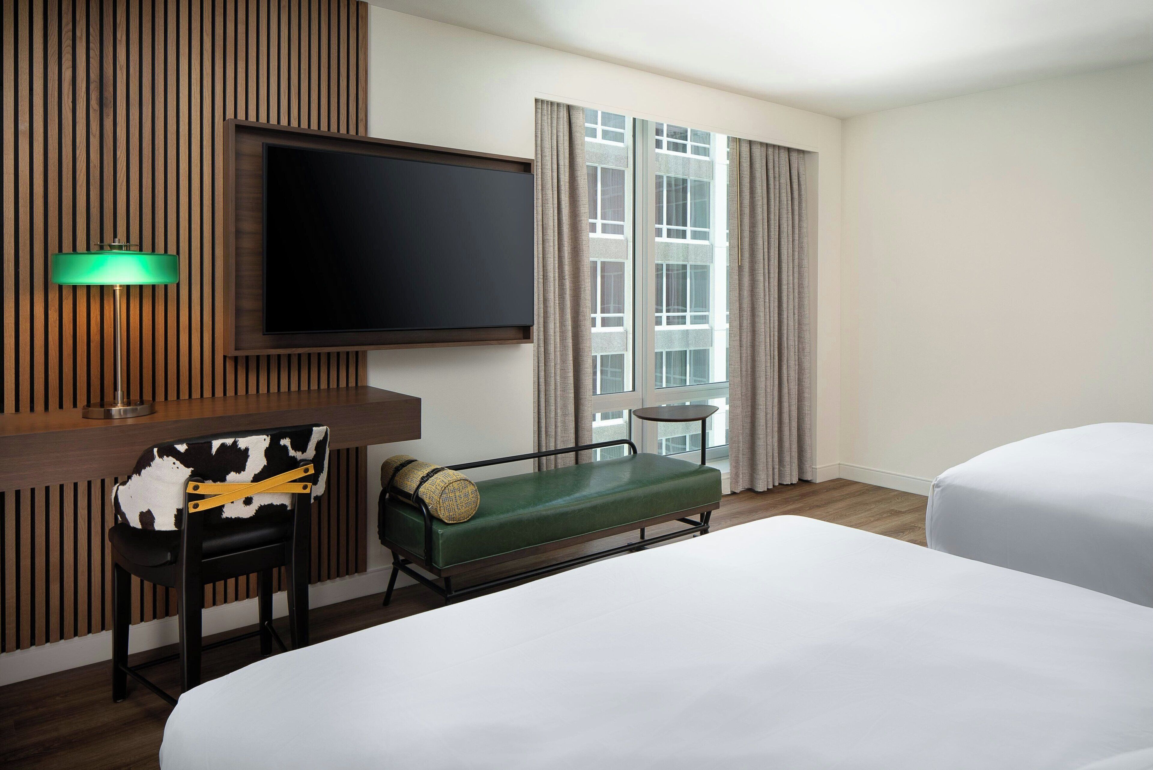 Una habitación de hotel con cama, escritorio, silla, televisor y ventana con cortinas.