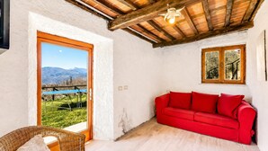 Una habitación con un sofá rojo, una silla de mimbre, techo de madera y vistas a montañas a través de una puerta.