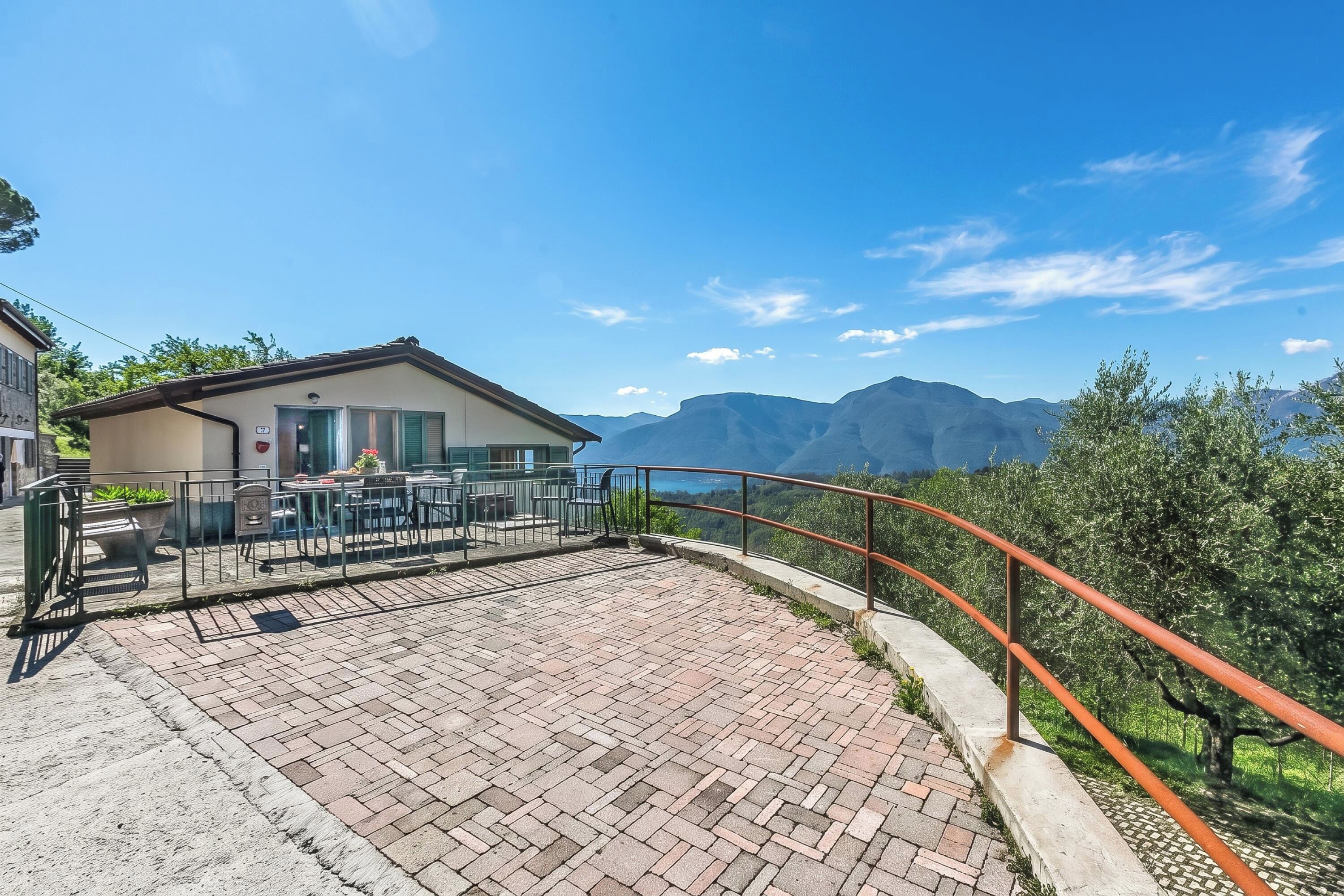 A patio area with a view of mountains, a building with a door and windows, and a railing.