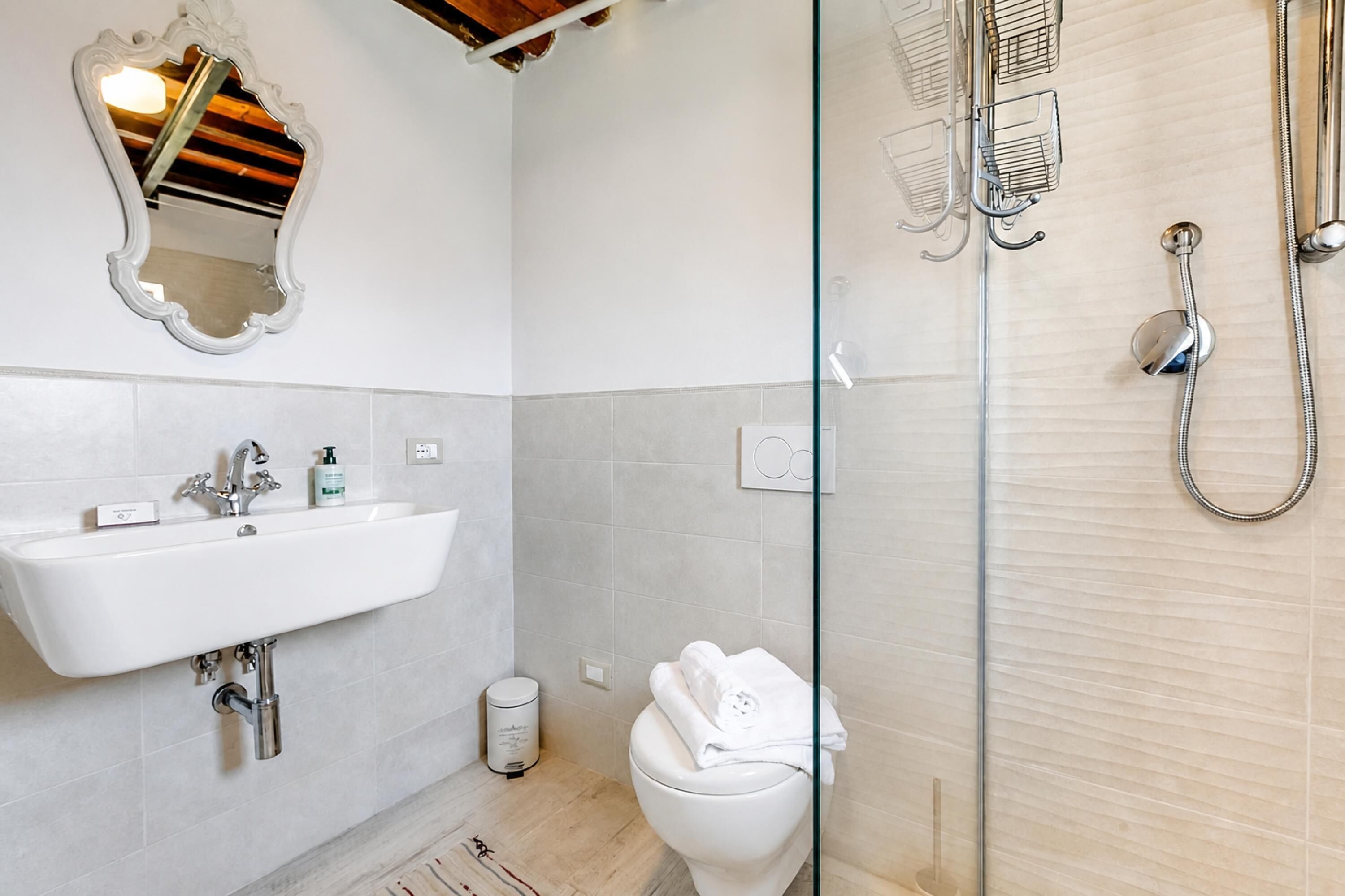 Une salle de bain avec un lavabo blanc, un miroir, des toilettes et une douche à parois de verre.