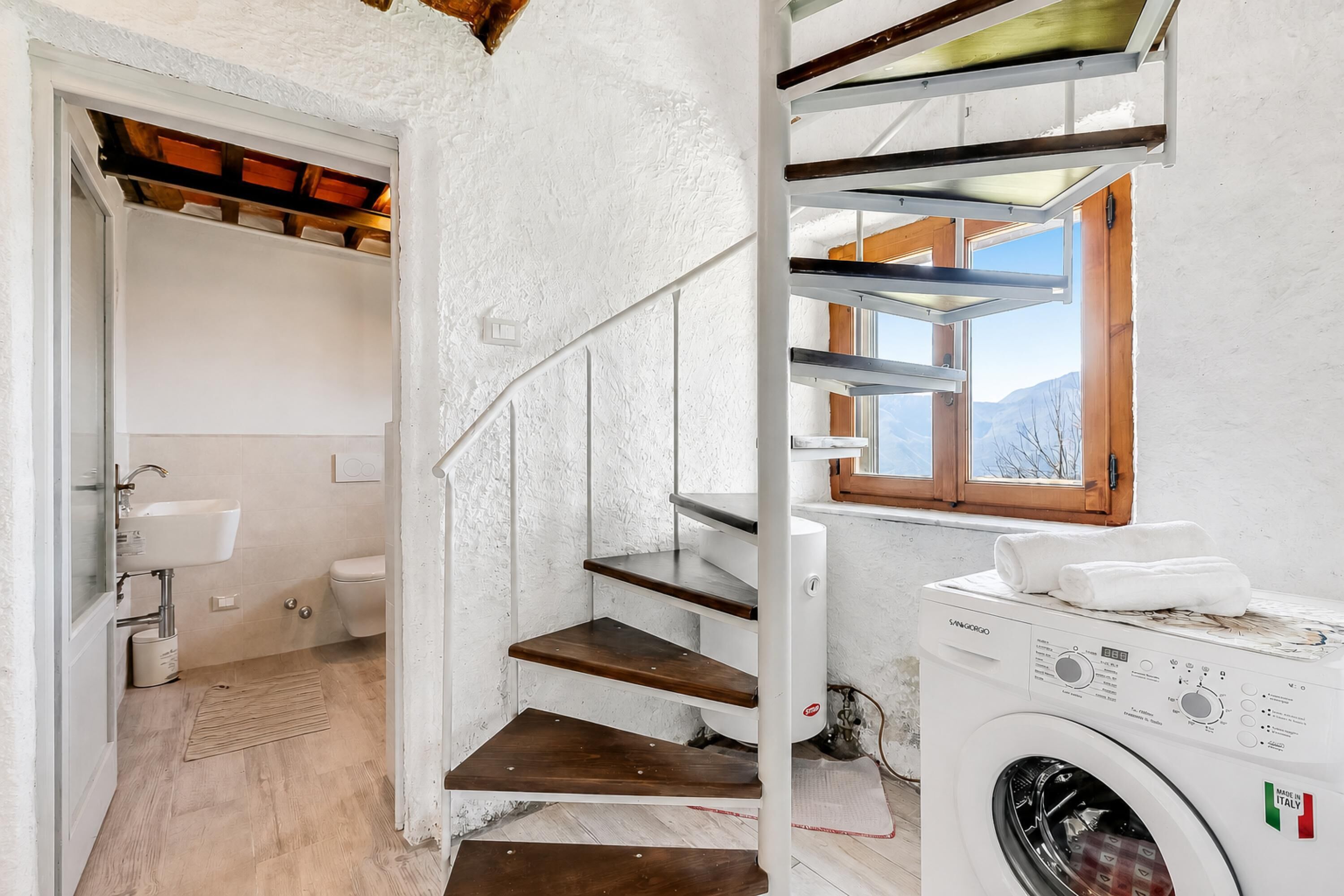 Une buanderie équipée d’un lave-linge, d’un escalier en bois et d’une fenêtre donnant sur les montagnes.