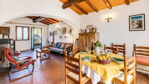 Un comedor con una mesa lista para cuatro, sillas de madera, un sofá y una cocina al fondo.
