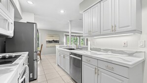 A modern kitchen with white cabinetry, stainless appliances, and a tiled floor. - Tropical Escape–Private Pool Home Near the Sand Hy Tee on Longboat Key by RVA (Longboat Key)