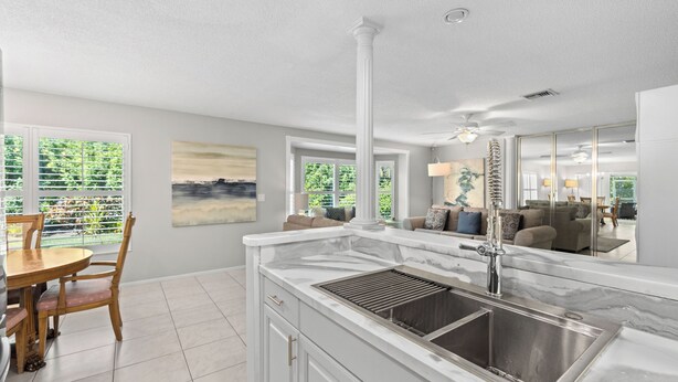 A modern kitchen with a marble countertop, stainless steel sink, and a dining area with a wooden table and chairs. - Tropical Escape–Private Pool Home Near the Sand Hy Tee on Longboat Key by RVA (Longboat Key)