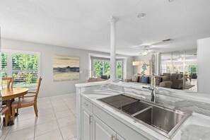 A modern kitchen with a marble countertop, stainless steel sink, and a dining area with a wooden table and chairs. - Tropical Escape–Private Pool Home Near the Sand Hy Tee on Longboat Key by RVA (Longboat Key)