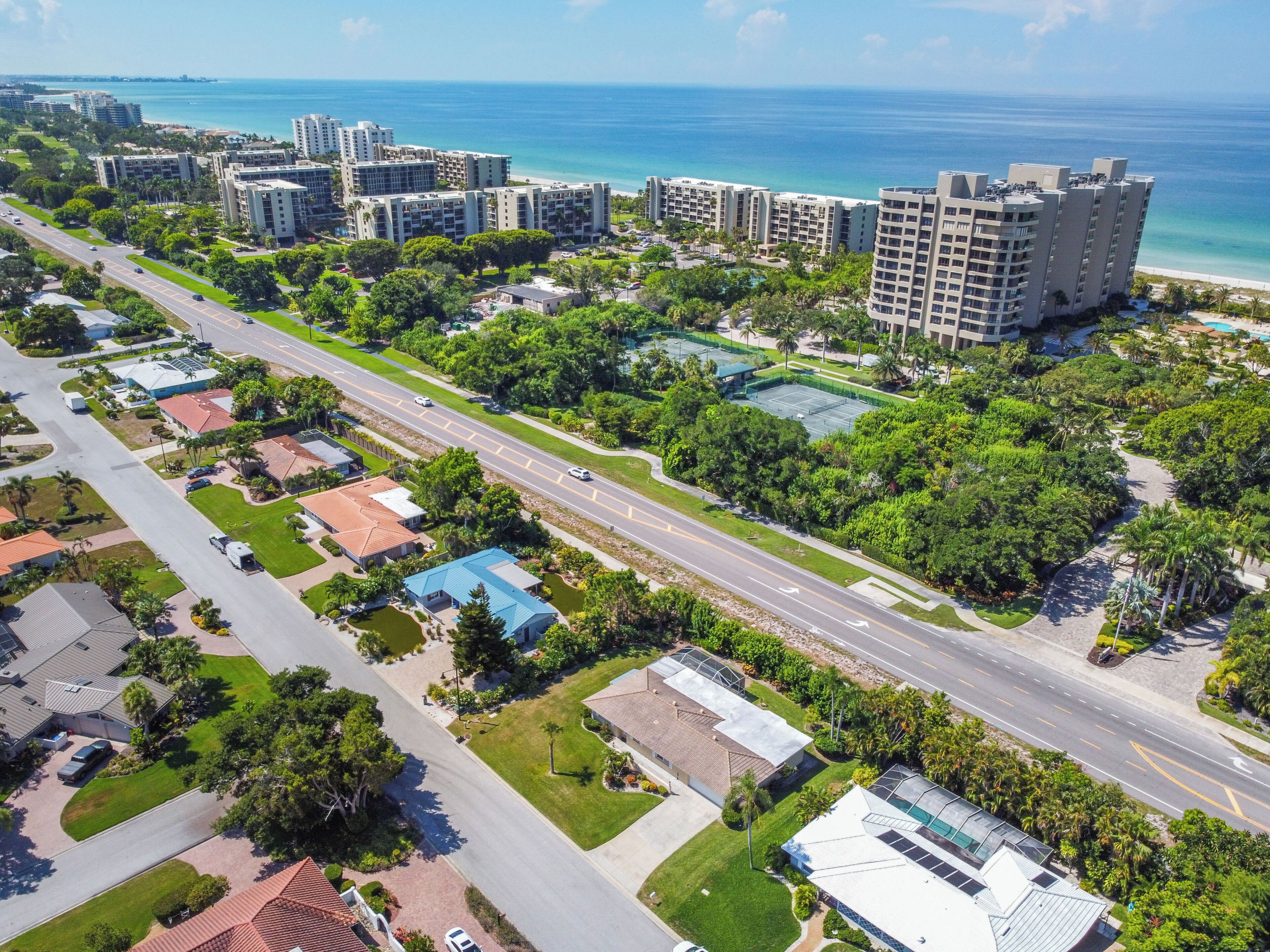 An aerial view of a coastal residential area with multiple high-rise buildings, a main road, and a beach in the background.
