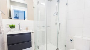 Un baño moderno con ducha de vidrio, lavamanos blanco con planta y un inodoro.