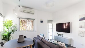 Una sala moderna con sofá, una mesa de comedor, sillas, un televisor y una planta en maceta.