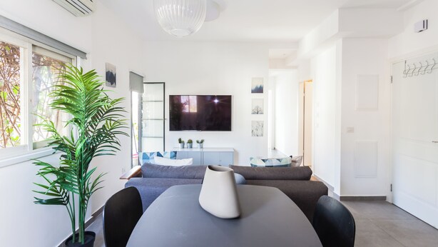 Una sala moderna con un televisor de pantalla plana grande, una mesa de comedor con un jarrón, un sofá y una planta en maceta.
