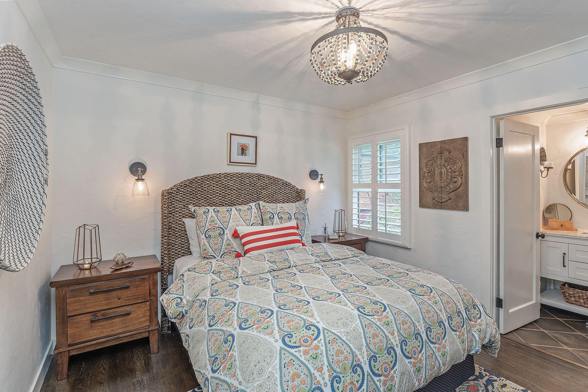 Une chambre à coucher comprenant un lit, des tables de chevet, un lustre et une porte donnant sur une salle de bain.