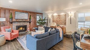 Een gezellige woonkamer met een open haard, houten lambrisering, een grote televisie en een comfortabele zithoek.