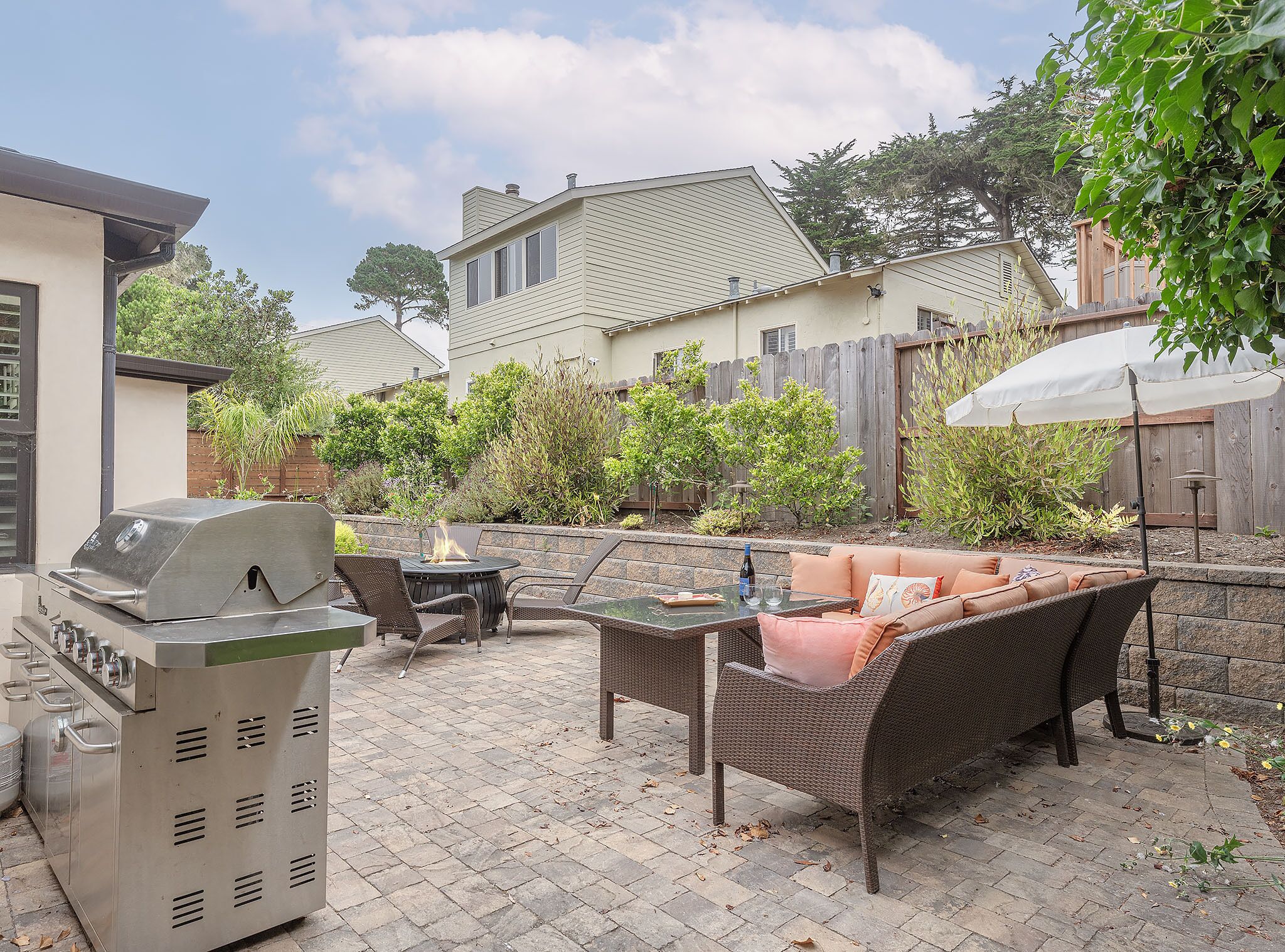 Une terrasse extérieure avec un barbecue, des meubles en osier et un parasol blanc.
