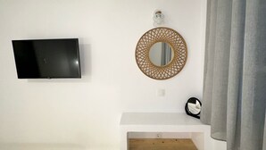 A room with a flat-screen TV mounted on the wall, a round mirror with a geometric frame, and a wooden shelf below. - Naousa Getaway 2 Bd Dreamy Island Escape (Paros)