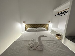 A neatly made bed with a swan towel arrangement, a wooden headboard, and wall-mounted lights. - Naousa Getaway 2 Bd Dreamy Island Escape (Paros)