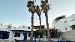 A modern building with white and blue exterior walls, palm trees, and a stone pathway. - Naousa Getaway 2 Bd Dreamy Island Escape (Paros)