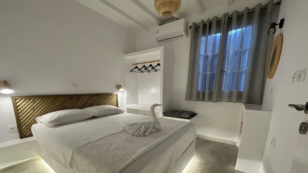A modern bedroom with a large bed, a bedside table, a wall-mounted air conditioning unit, and a window with curtains. - Naousa Getaway 2 Bd Dreamy Island Escape (Paros)
