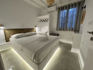 A modern bedroom with a large bed, a bedside table, a wall-mounted air conditioning unit, and a window with curtains.