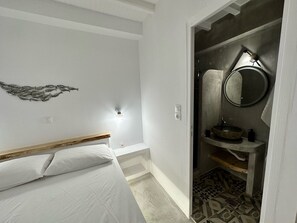 A bedroom with a bed, a wall-mounted light, and a bathroom with a sink and mirror.