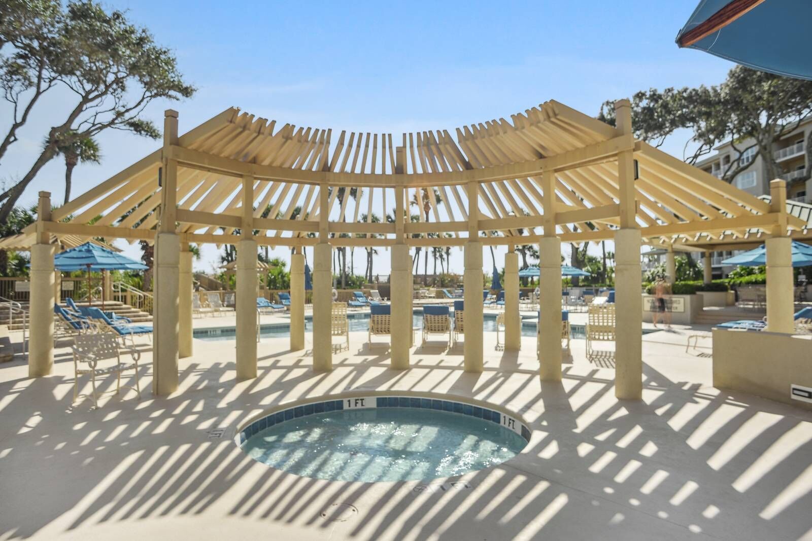 A pool area with a wooden pergola, lounge chairs, and a hot tub.