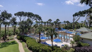 A resort pool area with palm trees, lounge chairs, and a view of the ocean. - Oceanfront luxury new to Island Getaway -amazing views  great weeks available (Hilton Head)