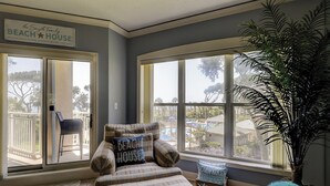 A room with a view of a beach, a chair, a couch, and a large plant. - Oceanfront luxury new to Island Getaway -amazing views  great weeks available (Hilton Head)