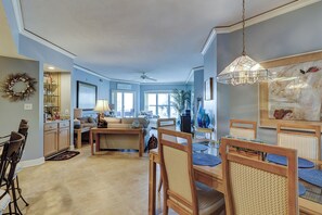 A spacious living room with a dining area, a kitchen, and a large window providing natural light.