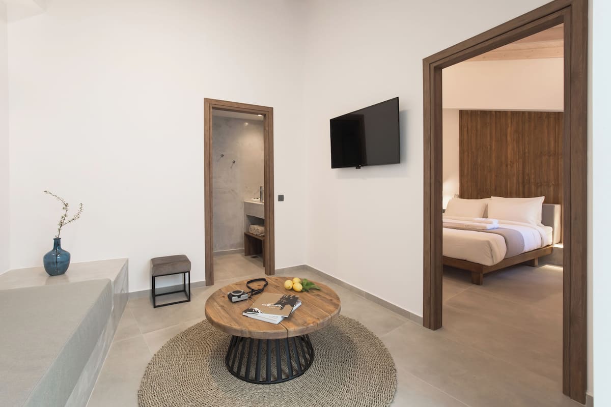 A modern hotel room with a round wooden table, a blue vase, and a bed with a wooden headboard.