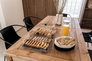 Una mesa de madera con una vitrina de vidrio que contiene pan rebanado, una jarrón de vidrio con jugo de naranja y una cesta de pan integral.