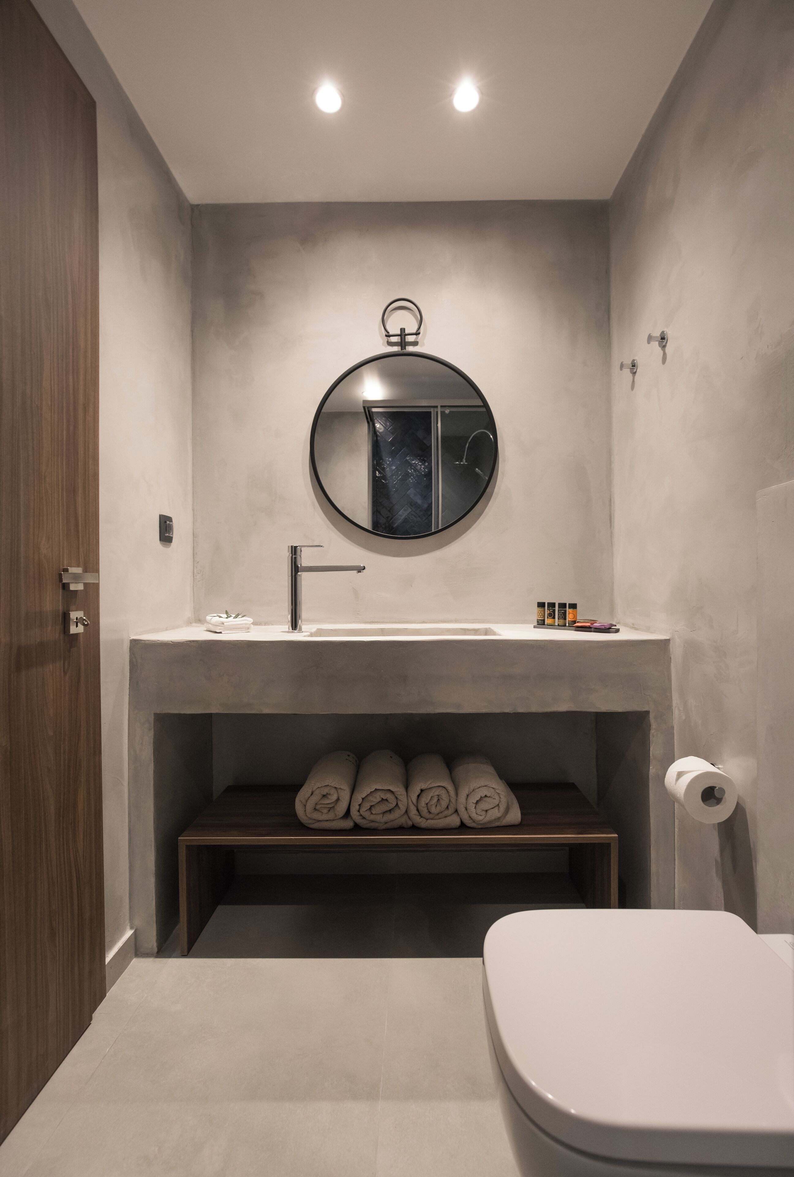 A modern bathroom with a round mirror, a sink, and a toilet.
