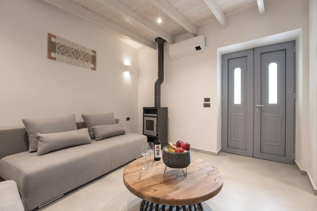 A modern living room with a sofa, a round wooden table with a fruit basket and a bottle, and a grey double door.