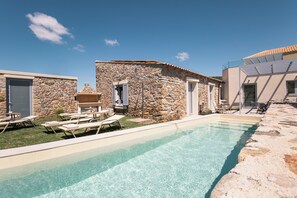 Un edificio de piedra con piscina, asientos al aire libre y una estructura moderna con tejado inclinado.