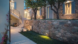 Un muro de piedra con una escalera que conduce a una puerta blanca, un árbol con frutos anaranjados y un pequeño jardín.