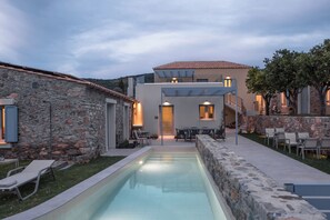 Una casa moderna con fachada de piedra, piscina y mobiliario de exterior.