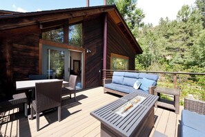 Una cabaña de madera con terraza, una mesa, sillas, un sofá y una chimenea.