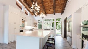 Une cuisine moderne avec des meubles blancs, un grand îlot central, des tabourets de bar et un lustre.