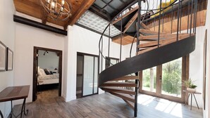 Une pièce spacieuse dotée d’un plancher en bois, d’un escalier en colimaçon et d’un lit offrant une vue sur la verdure environnante.