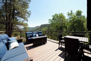 Una terraza con sofá, una mesa y sillas, con vista a un paisaje montañoso.