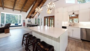 Une cuisine spacieuse dotée d’un grand îlot central, de meubles blancs et d’un plafond en bois.