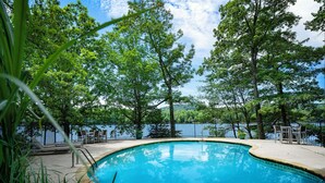 Une piscine dont la profondeur maximale est de 2,7 mètres, indiquée par un panneau, entourée d’arbres et offrant une vue sur une étendue d’eau.